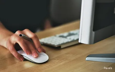 Nahaufnahme einer Hand auf einer Computermaus, die zusätzlich einen Stift hält.