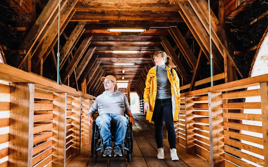 Ein Paar besichtigt das Gradierwerk in Bad Sassendorf. Er sitzt im Rollstuhl und sie läuft neben ihm.