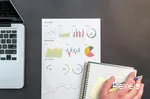 Ein Zettel mit mehreren Graphen liegt zwischen einem Laptop und einem Block mit Stift.