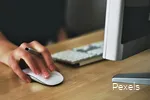 Nahaufnahme einer Hand auf einer Computermaus, die zusätzlich einen Stift hält.