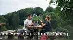 Ein Paar macht eine Wanderpause auf einer Sauerland-Bank und isst. Im Hintergrund sieht man die Meinhardus-Schanze.