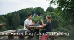Ein Paar macht eine Wanderpause auf einer Sauerland-Bank und isst. Im Hintergrund sieht man die Meinhardus-Schanze.